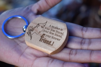 A wooden keychain with an engraving of a silhouette of a woman's face adorned with flowers and a heartfelt message, held gently in an open palm.