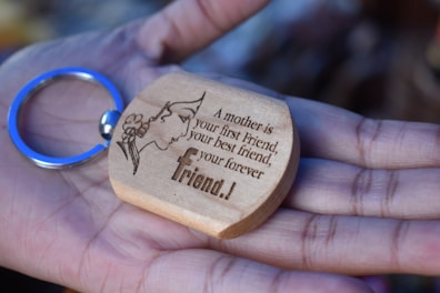 A wooden keychain with an engraving of a silhouette of a woman's face adorned with flowers and a heartfelt message, held gently in an open palm.