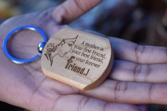 A wooden keychain with an engraving of a silhouette of a woman's face adorned with flowers and a heartfelt message, held gently in an open palm.