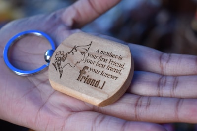 A wooden keychain with an engraving of a silhouette of a woman's face adorned with flowers and a heartfelt message, held gently in an open palm.