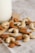 A close-up of scattered almonds and cashews placed on a light-colored fabric surface near a wooden board. The edge of a glass jar is visible on the left side.