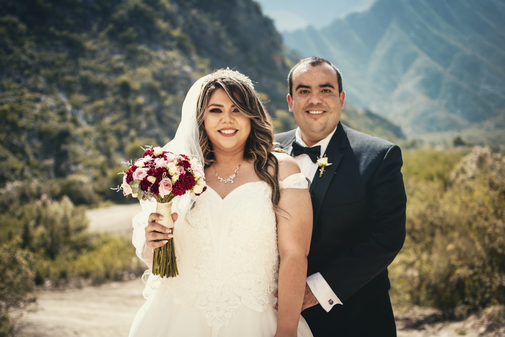 man in black suit and woman in white wedding dress holding bouquet of flowers