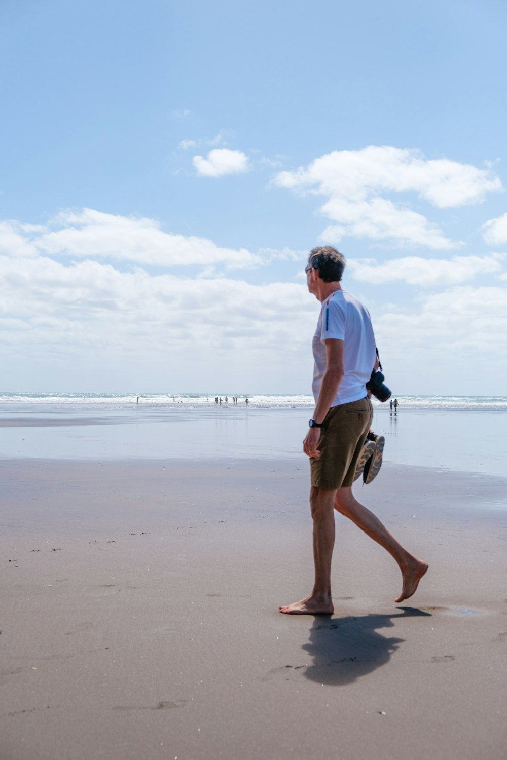 man in white shirt and brown shorts holding black and white dog on beach during daytime