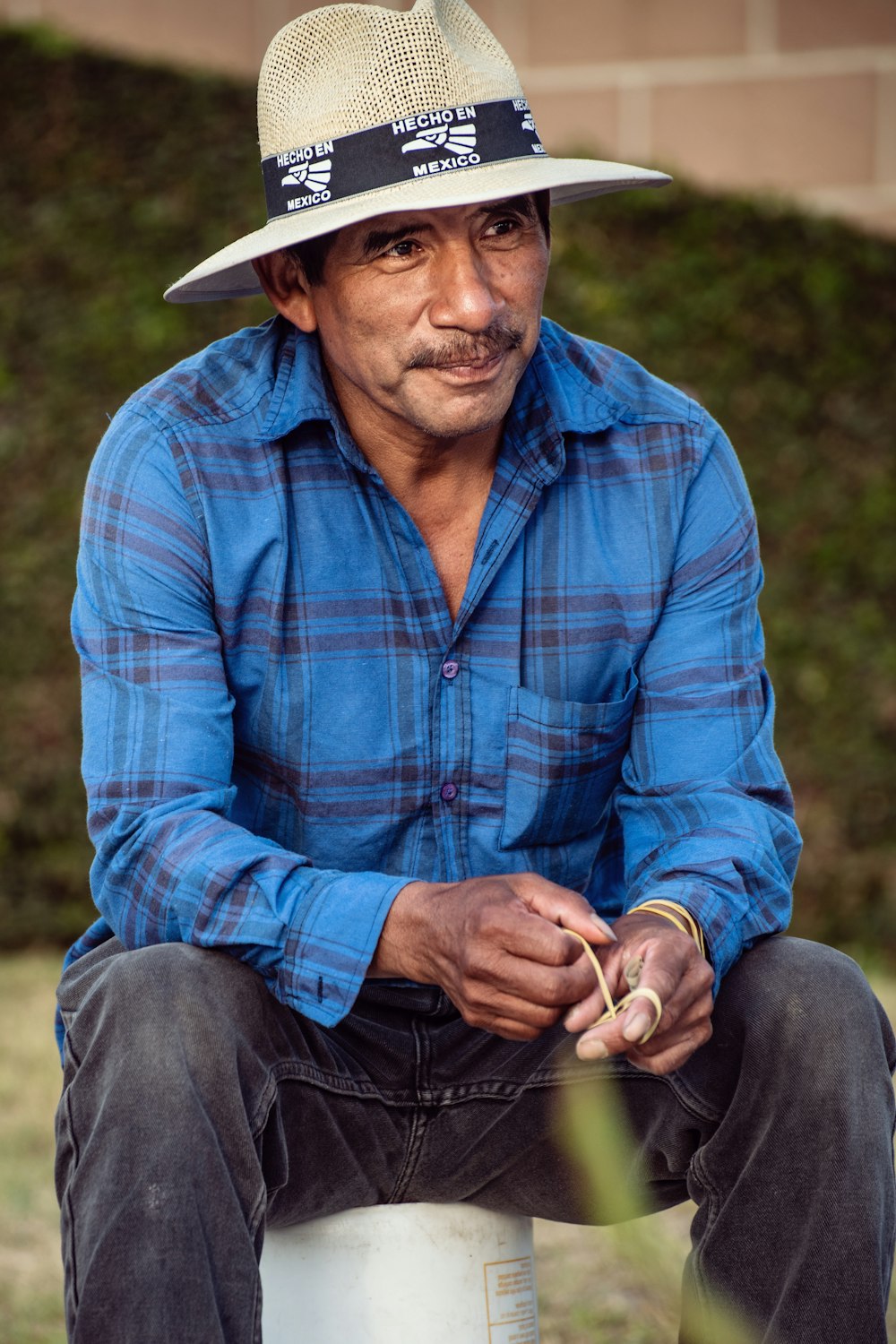 man in blue and red plaid dress shirt wearing white cowboy hat sitting on green grass