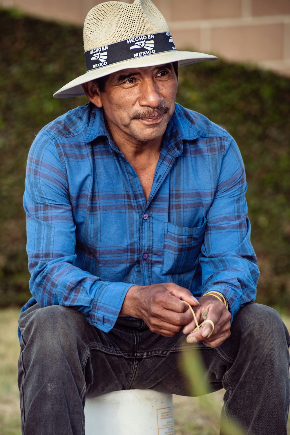 hombre con camisa de vestir a cuadros azul y rojo con sombrero de vaquero blanco sentado en la hierba verde