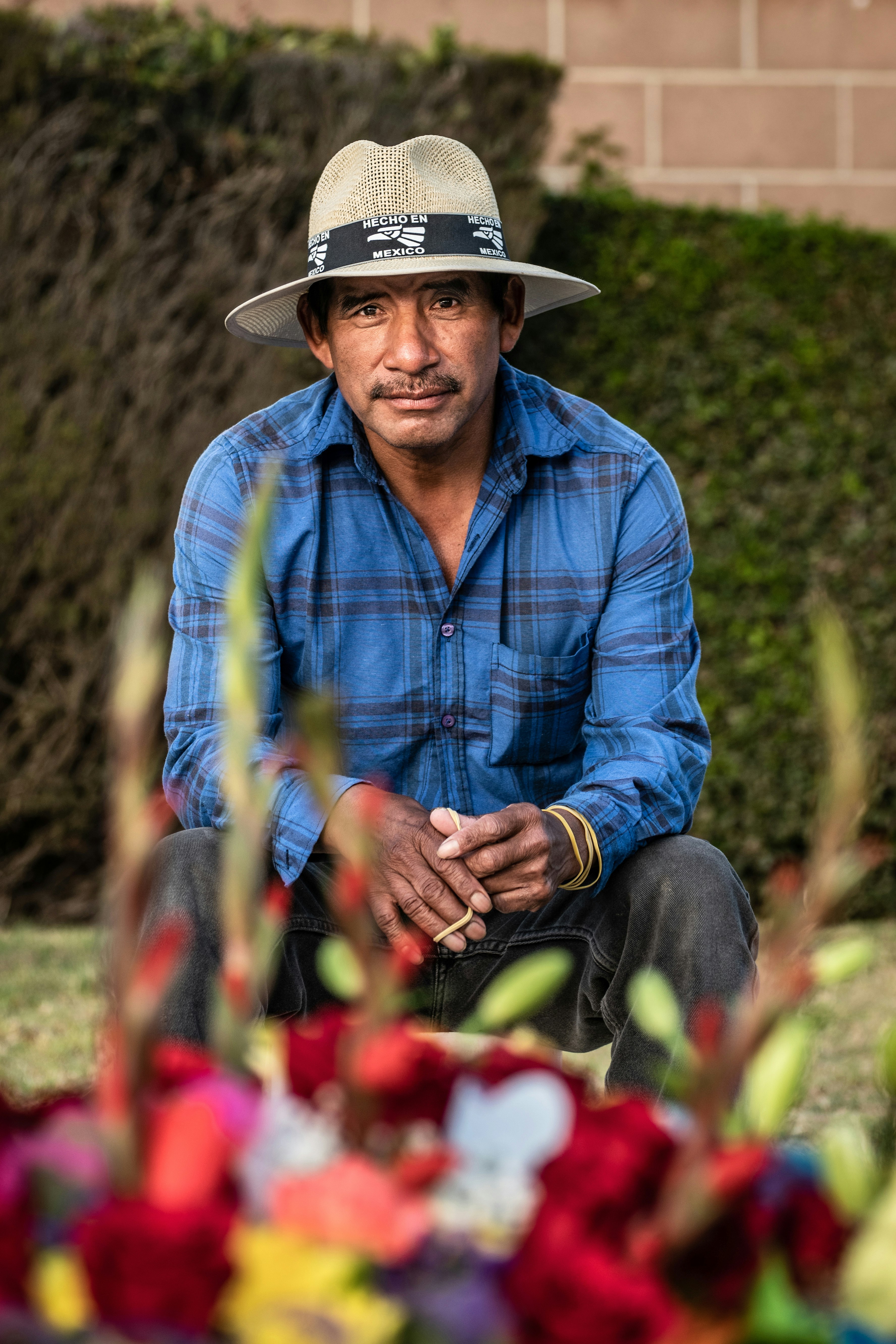 man in blue and white plaid dress shirt wearing brown cowboy hat sitting on red flower