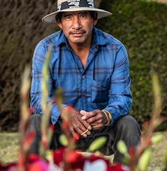 man in blue and white plaid dress shirt wearing brown cowboy hat sitting on red flower