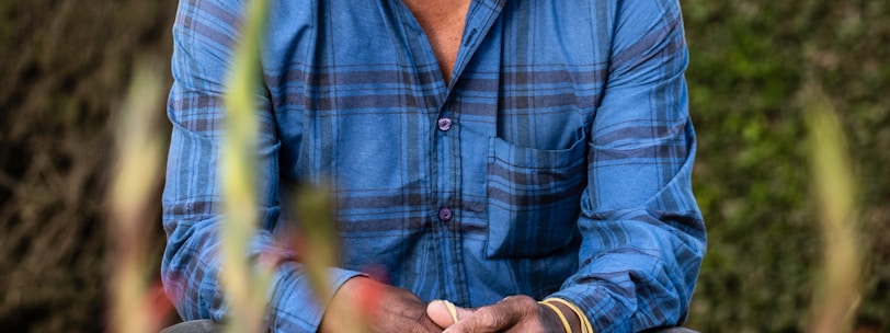 man in blue and white plaid dress shirt wearing brown cowboy hat sitting on red flower