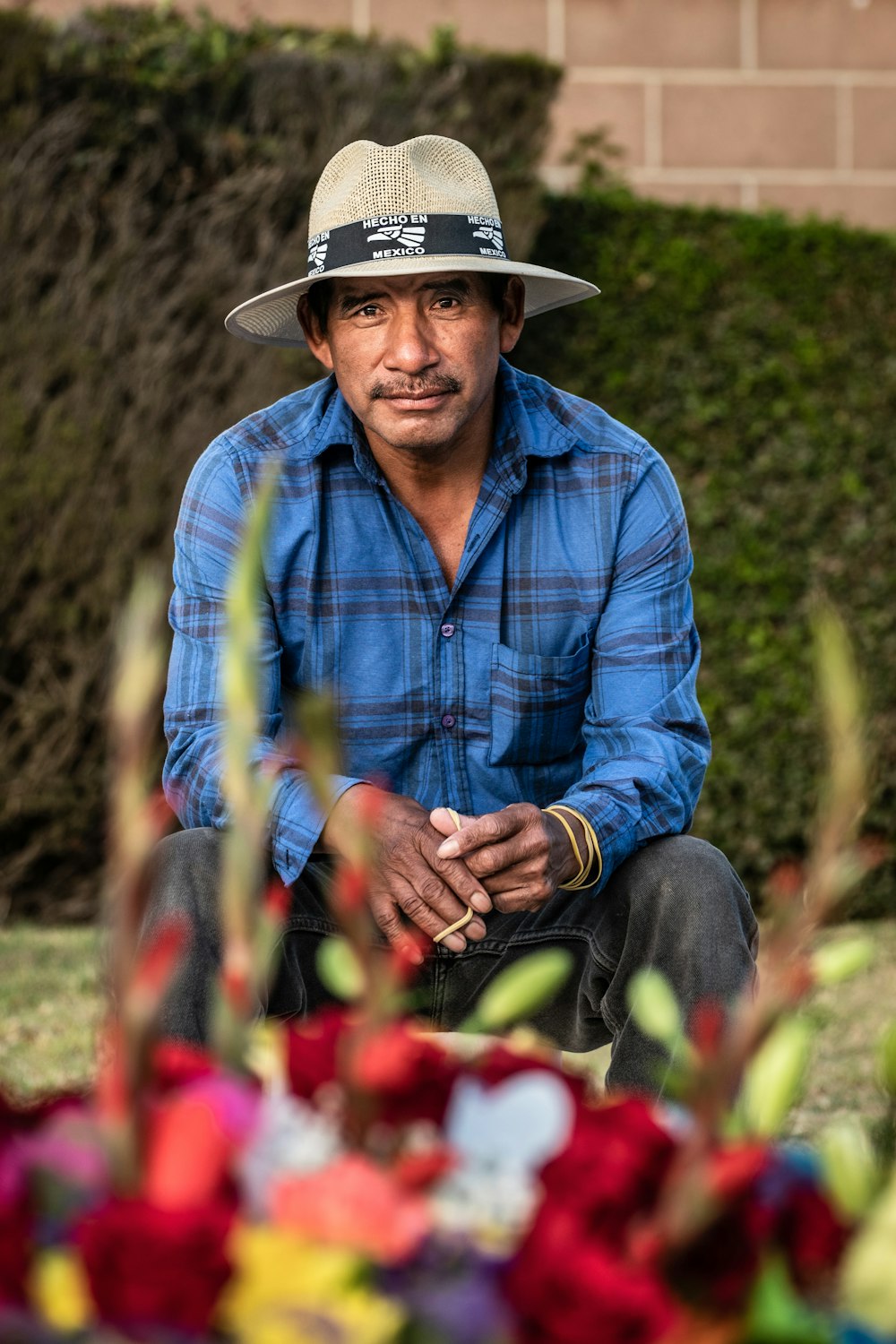 homme en chemise à carreaux bleu et blanc portant un chapeau de cow-boy marron assis sur une fleur rouge