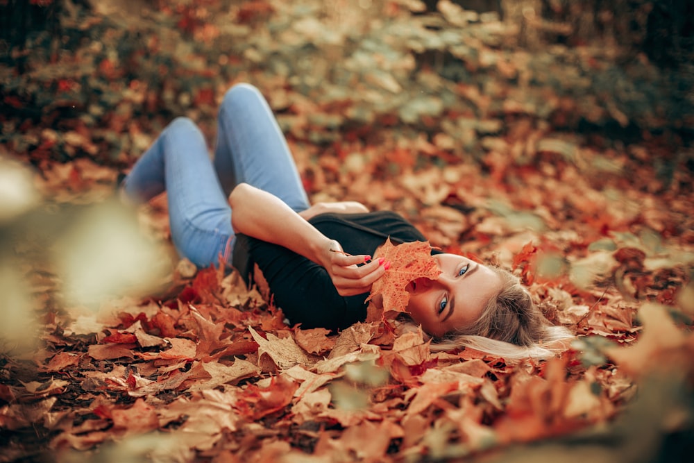 woman in black long sleeve shirt and blue denim jeans lying on brown leaves