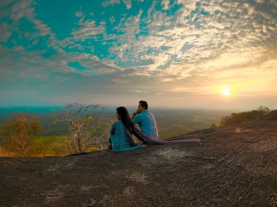 man and woman sitting on brown dirt road during daytime eve teams background