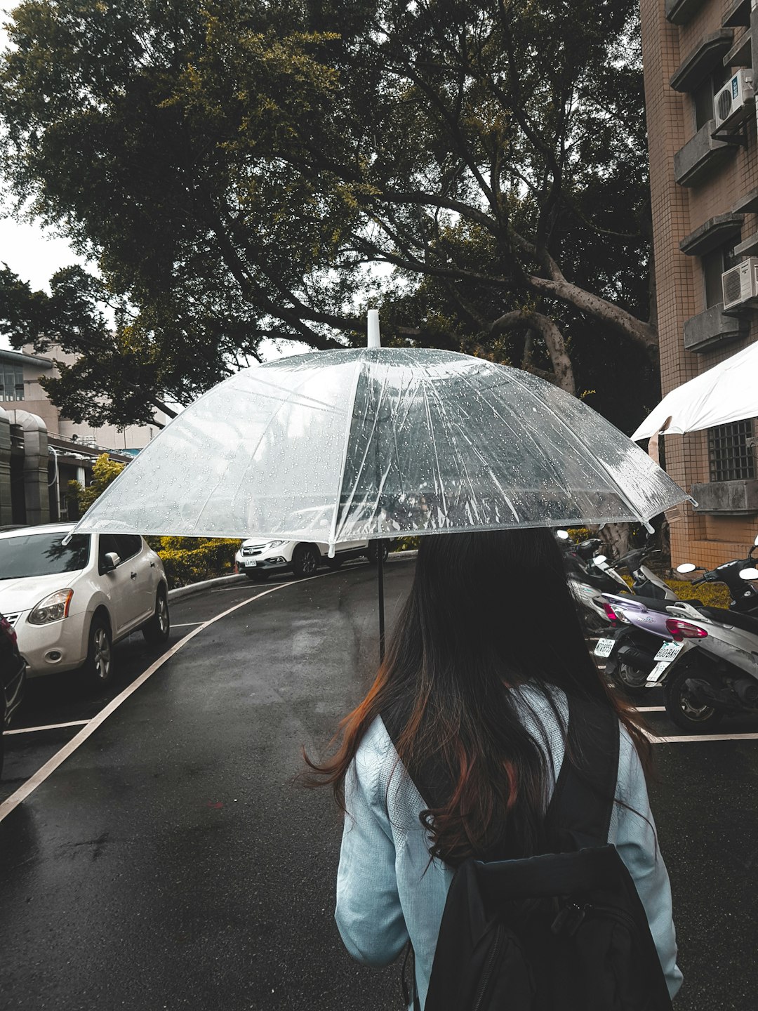 woman in blue denim jacket holding umbrella walking on street during daytime