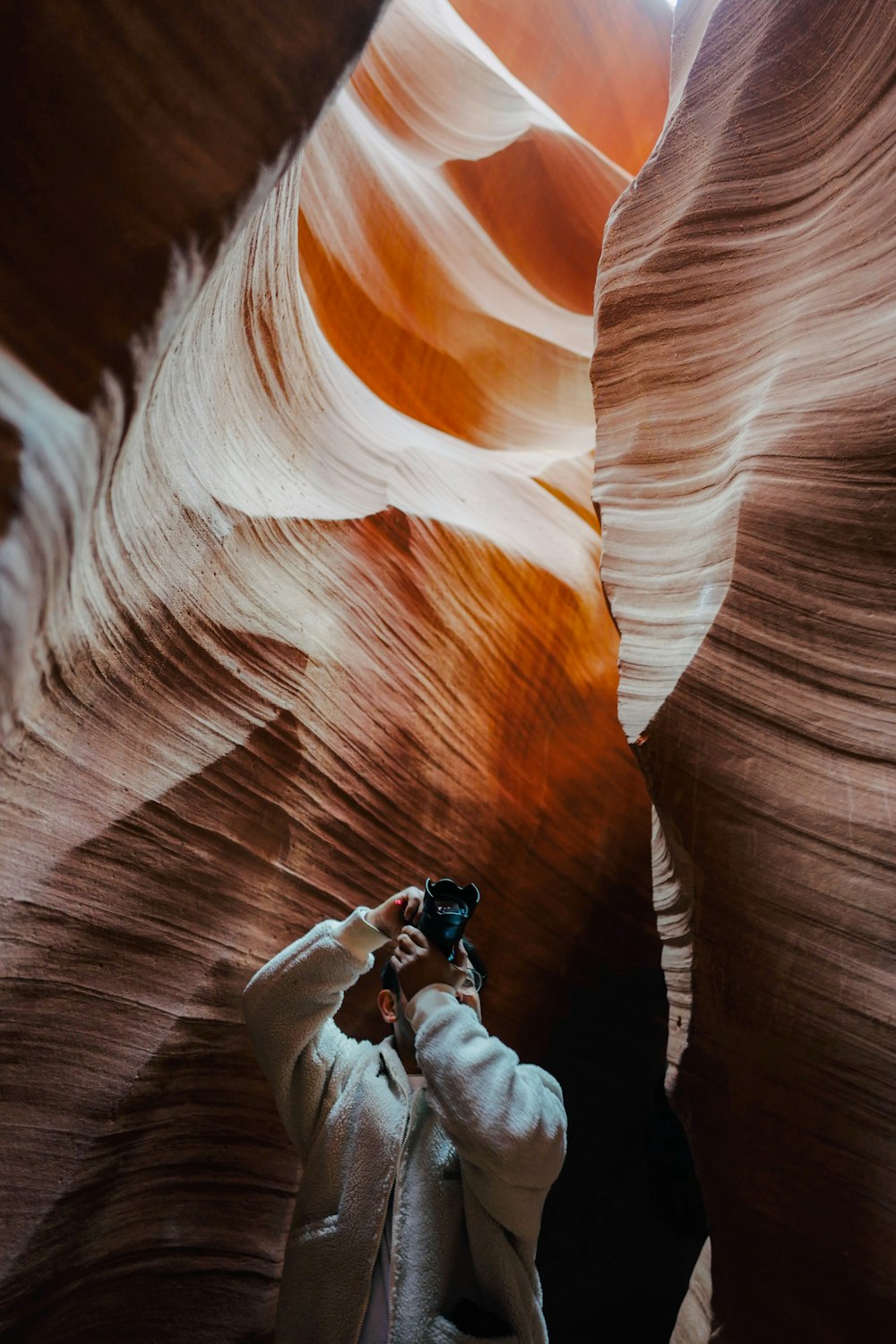 man in white jacket and black pants sitting on brown rock formation during daytime