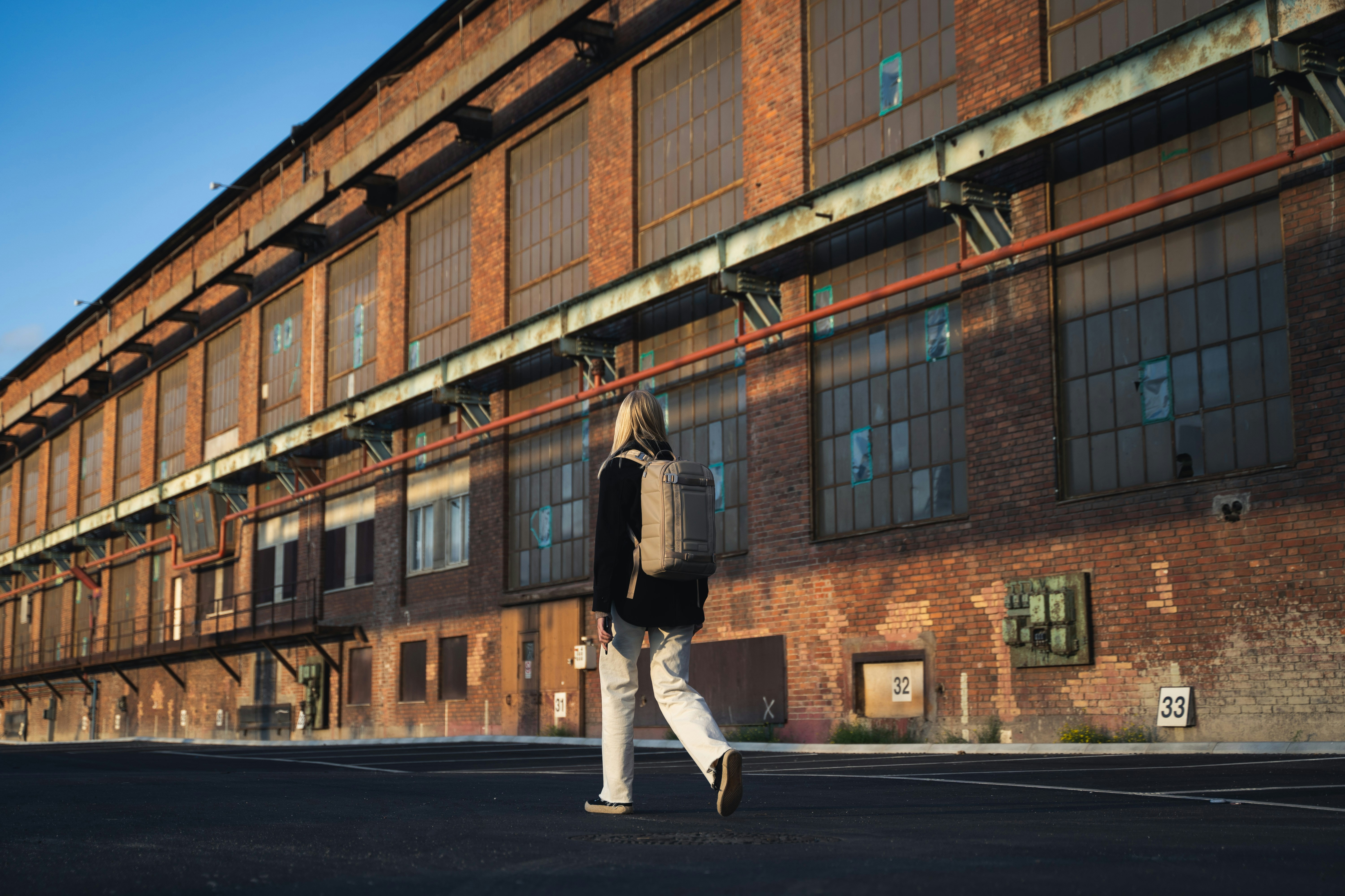 man in black jacket and white pants walking on sidewalk during daytime