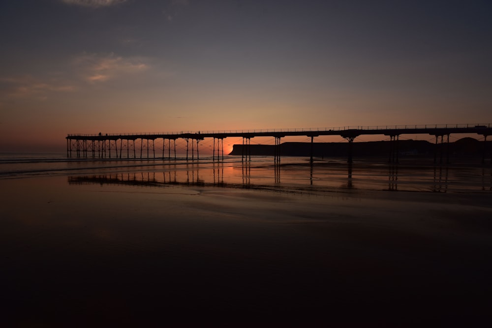 silhouette of bridge over body of water during sunset