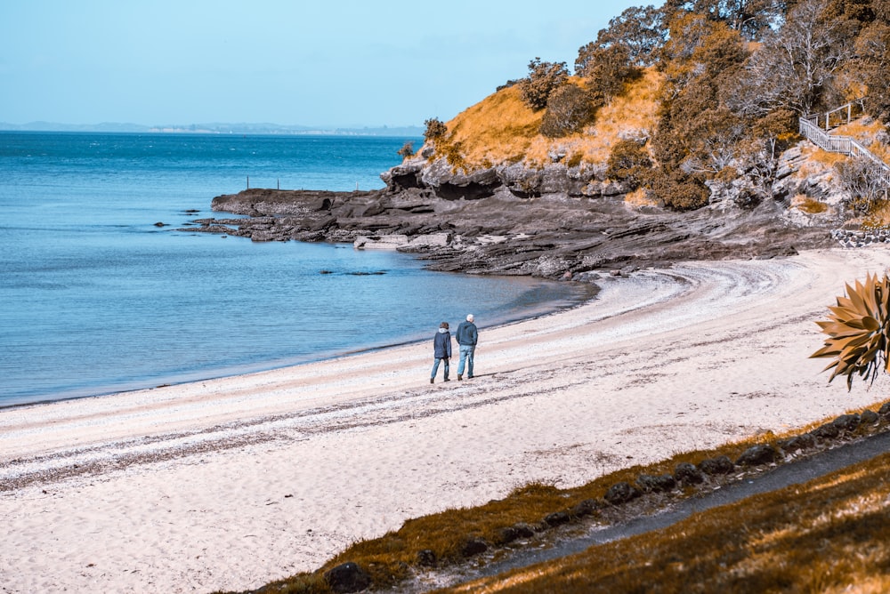 couple walking on beach shore during daytime