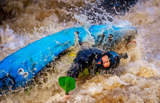 man in black wet suit lying on blue surfboard on water during daytime in Crana River Ireland