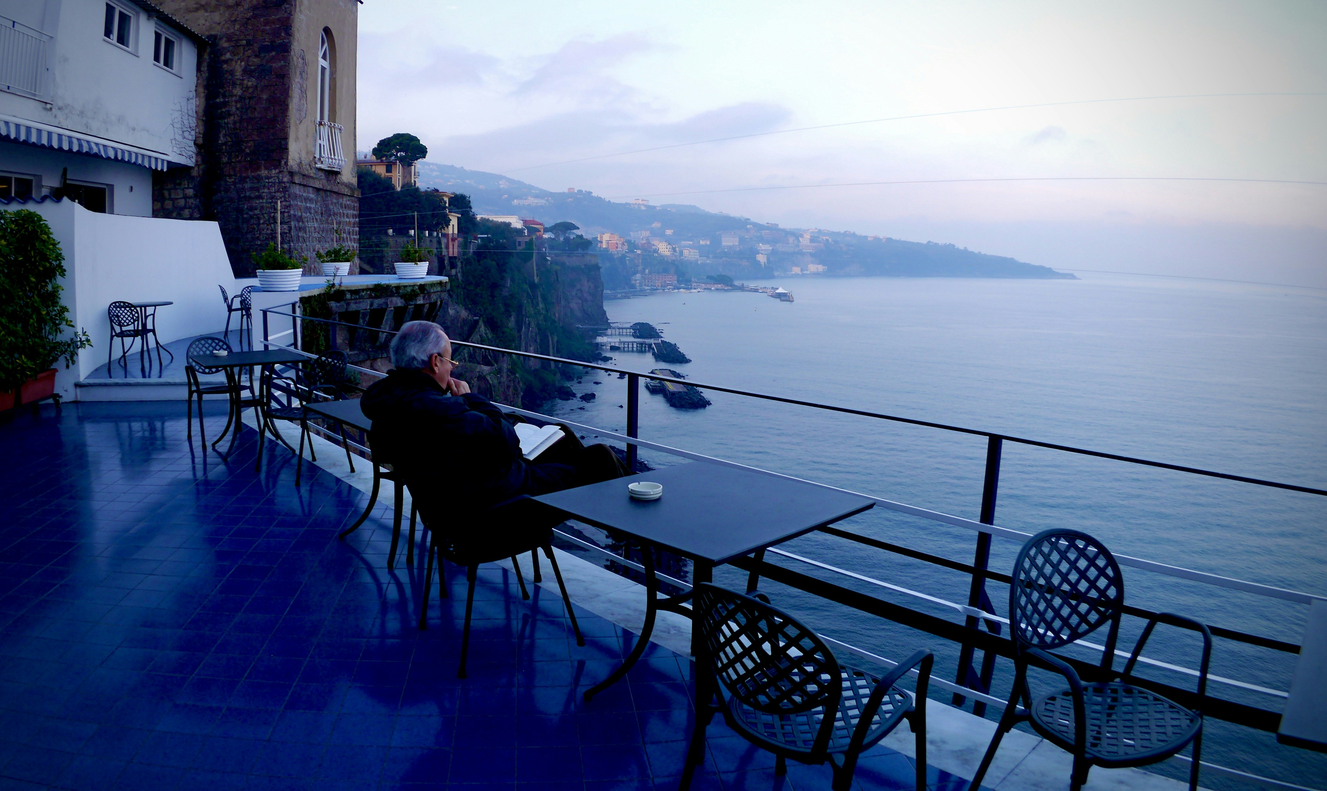 man in black jacket sitting on black chair near body of water during daytime