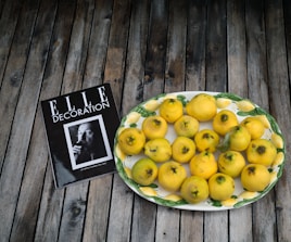 A decorative plate filled with yellow quinces is placed on a wooden surface beside a magazine titled 'ELLE Decoration' featuring a black and white portrait.