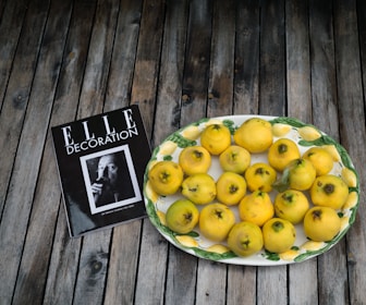 A decorative plate filled with yellow quinces is placed on a wooden surface beside a magazine titled 'ELLE Decoration' featuring a black and white portrait.
