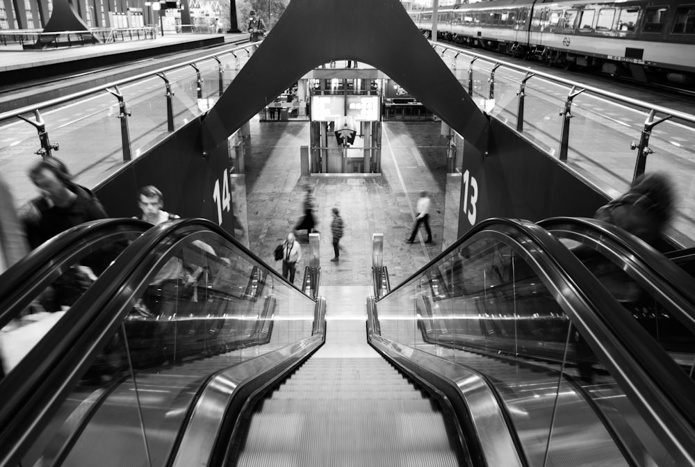 grayscale photo of people walking on escalator