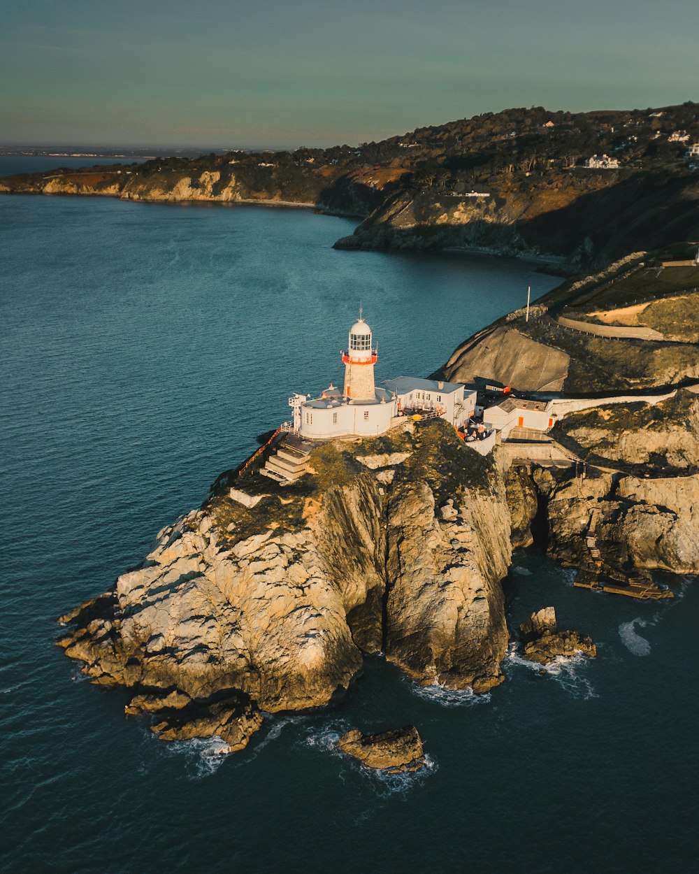 farol branco na formação rochosa marrom perto do corpo de água durante o dia