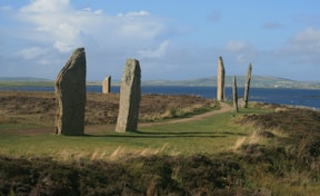 gray rock formation on green grass field under white clouds during daytime