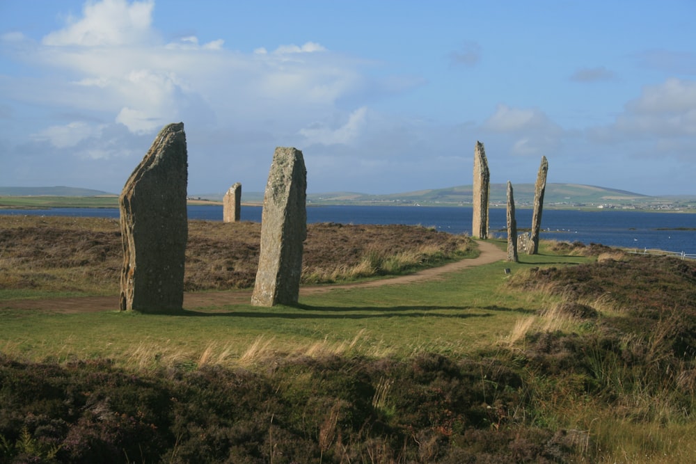 gray rock formation on green grass field under white clouds during daytime