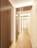 A modern hallway features a series of vertical wooden slats on the left, adding a contemporary architectural element. The space is well-lit with subtle overhead lighting, creating a warm and inviting atmosphere. The flooring is a light wood, complementing the overall neutral tones of the walls and ceiling.