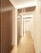 A modern hallway features a series of vertical wooden slats on the left, adding a contemporary architectural element. The space is well-lit with subtle overhead lighting, creating a warm and inviting atmosphere. The flooring is a light wood, complementing the overall neutral tones of the walls and ceiling.