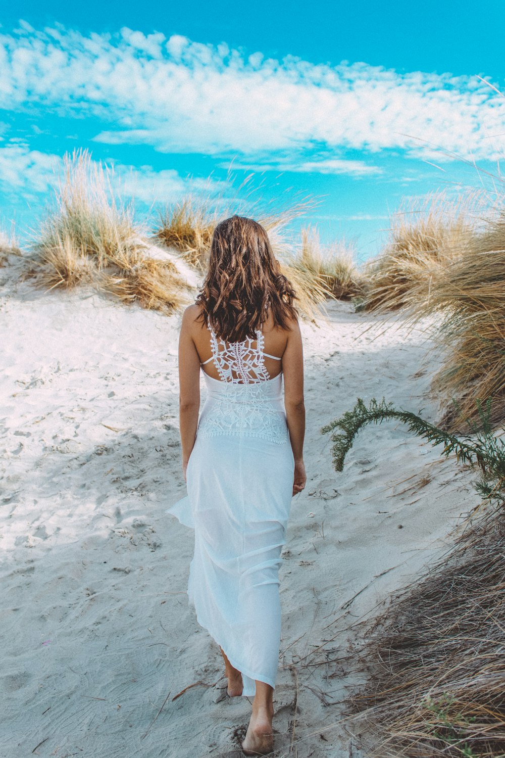 Frau im weißen Spaghettiträgerkleid, tagsüber auf weißem Sand stehend