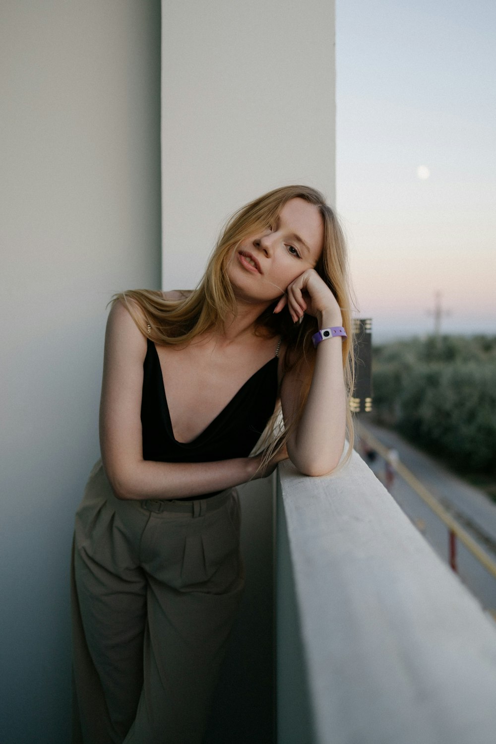 woman in black tank top and gray pants leaning on white wall