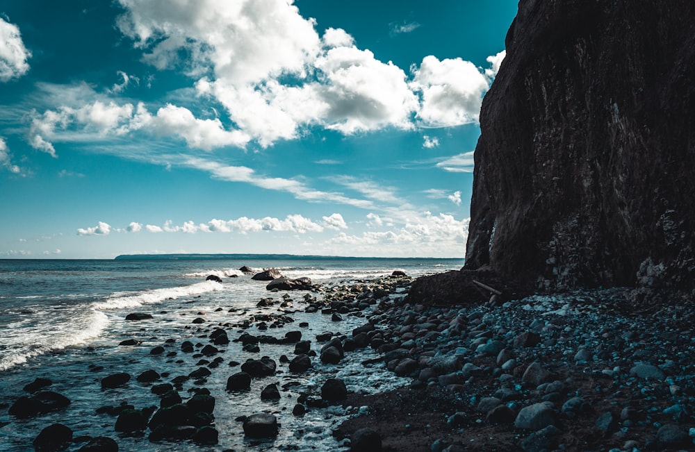 formazione rocciosa marrone vicino al mare sotto cielo nuvoloso blu e bianco durante il giorno