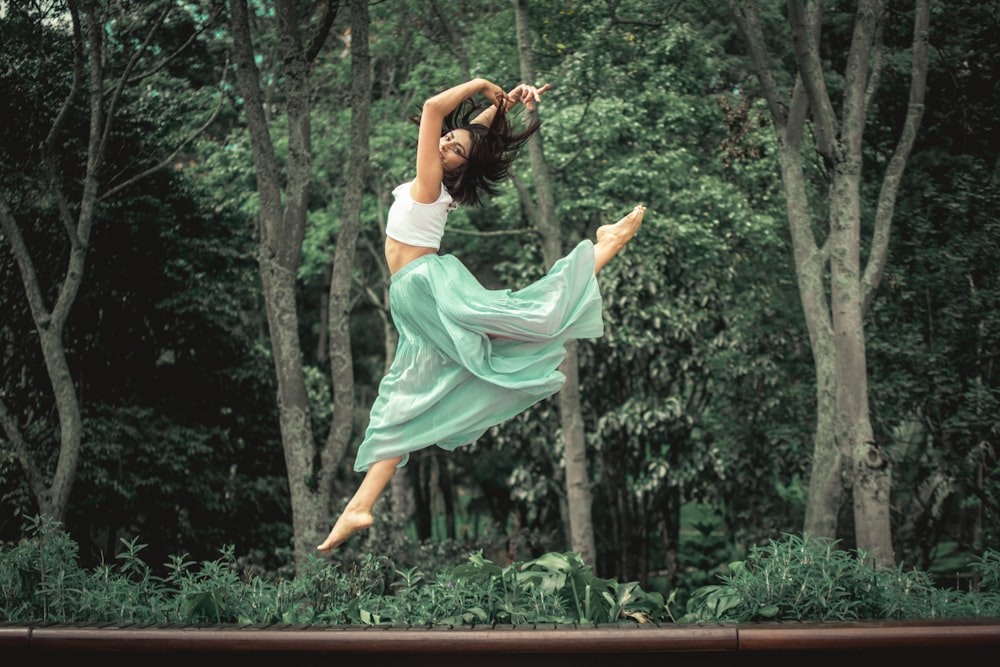 woman in white dress jumping on brown wooden fence during daytime