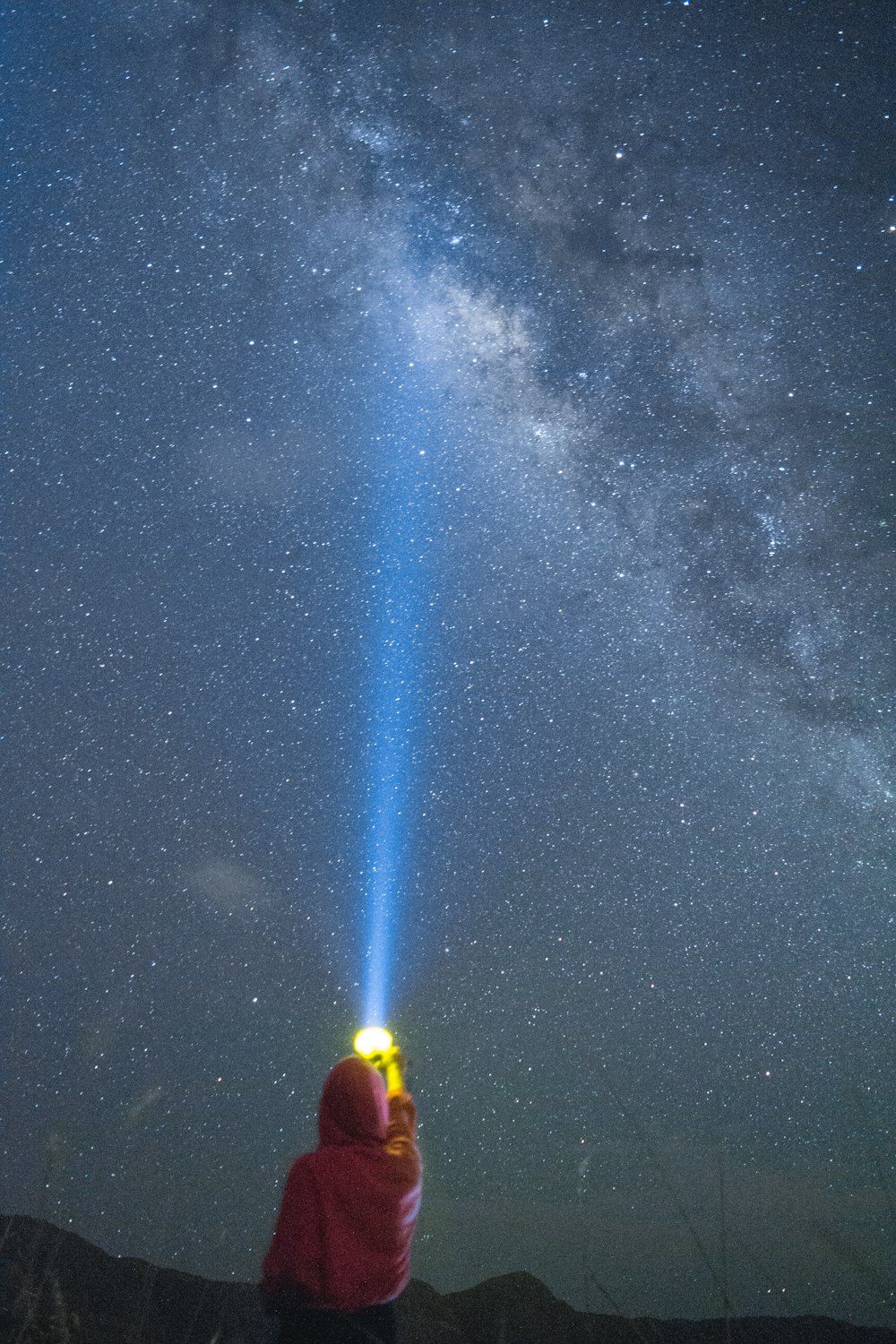 person in yellow jacket and blue denim jeans standing on ground under starry night