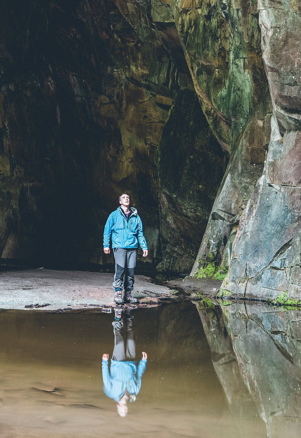 man in blue jacket and black pants standing on river