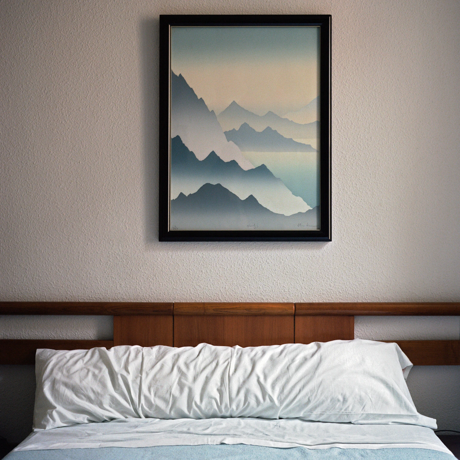 A framed mountain print in a black frame hanging above a bed