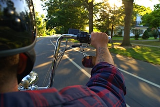 A rider wearing a helmet cruising through a tree-lined road on a sunny day.