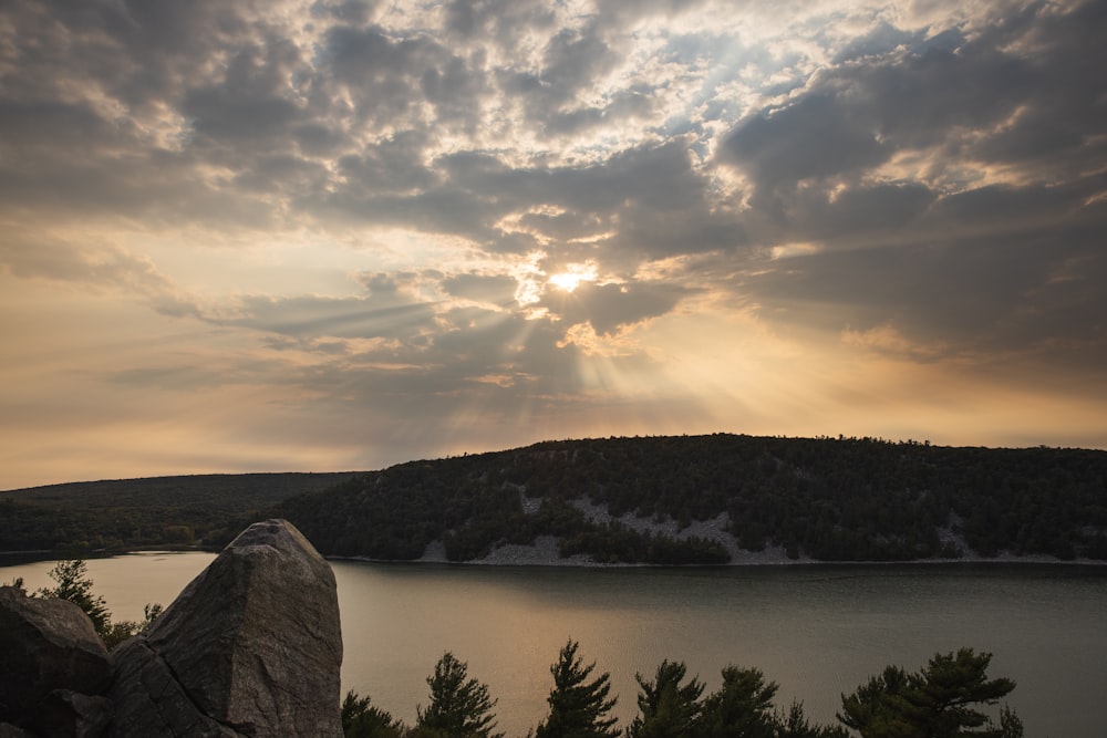 body of water near mountain under cloudy sky during daytime