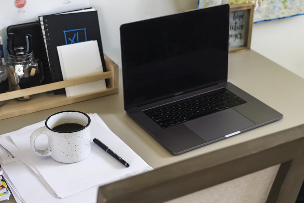 black laptop computer beside white ceramic mug on white table