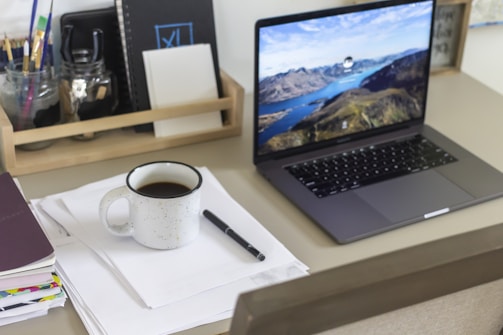 Modern office workspace with a laptop and notes on a wooden desk.