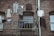 A brick facade with clothing hanging on a clothesline. Several items, including shirts, pants, and socks, are draped over the line and a metal railing, set against the rustic texture of the building's exterior.