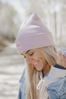 A young woman wearing a soft pink knitted beanie, smiling in a sunlit park.