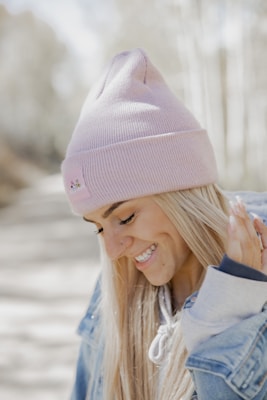 A young woman wearing a chunky knit beanie in soft pastel colors, smiling outdoors on a crisp autumn day.