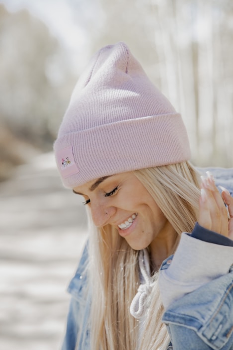 A young woman wearing a chunky knit beanie in soft pastel colors, smiling outdoors on a crisp autumn day.