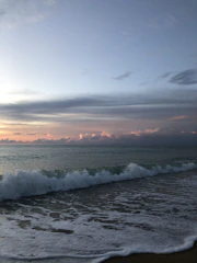 A serene coastal horizon at dusk highlighting gentle waves meeting an untouched sandy shore.