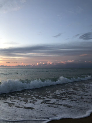 A serene coastal horizon at dusk highlighting gentle waves meeting an untouched sandy shore.