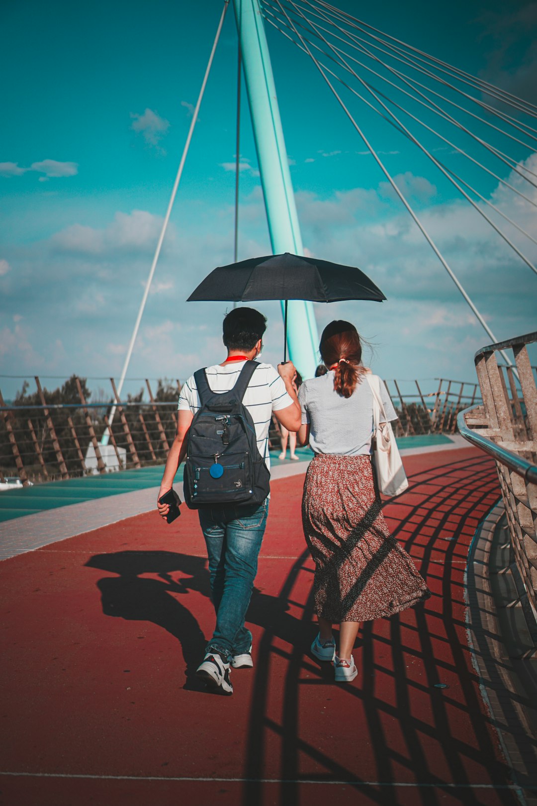 man and woman holding umbrella while walking on bridge