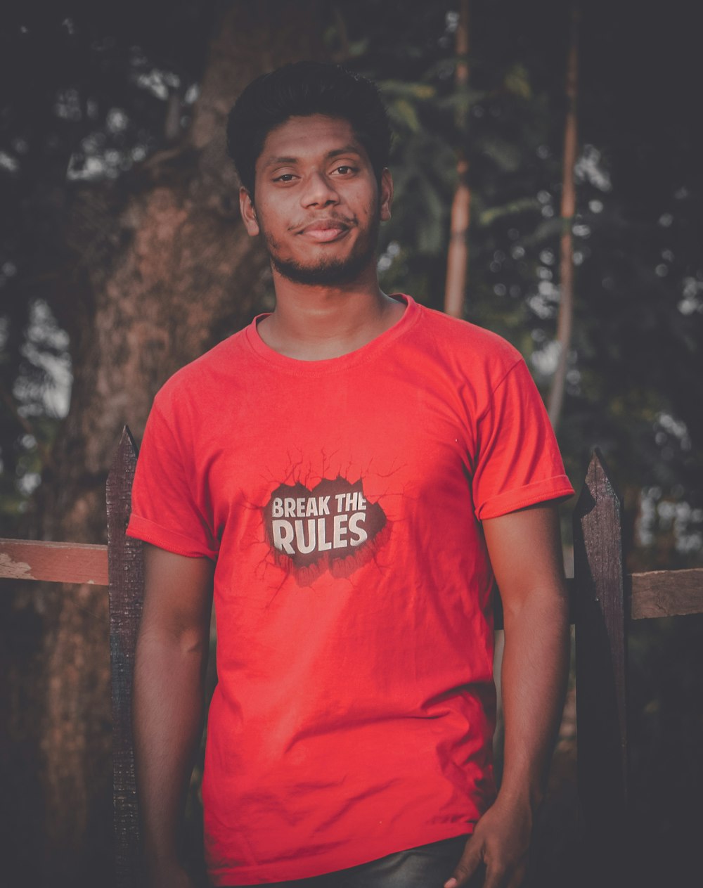 man in red crew neck t-shirt standing near brown wooden fence