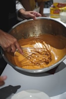 Hands mixing vibrant banana-based batter in a rustic wooden bowl.
